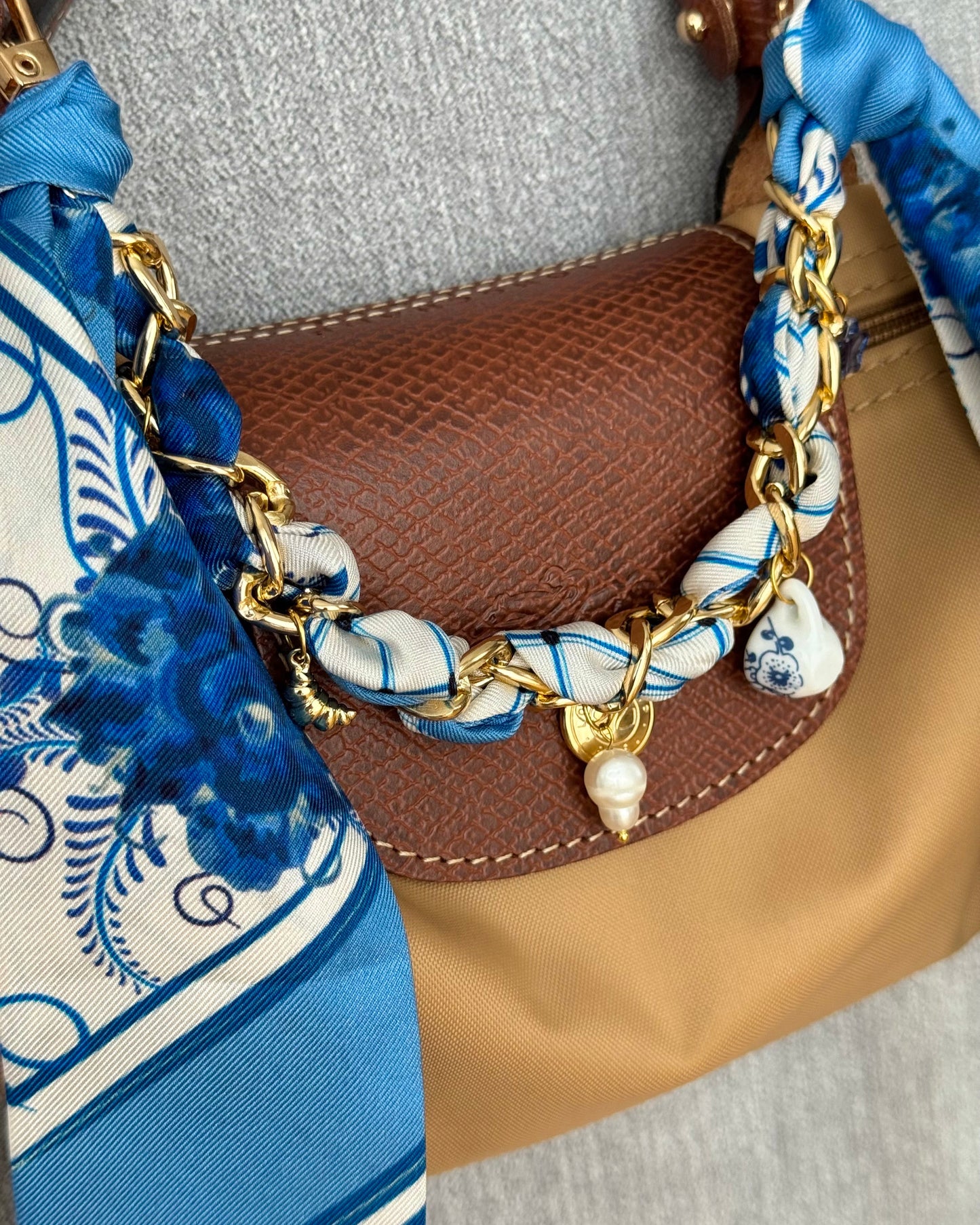 Brown handbag with a decorative chain and blue fabric strap featuring white patterns.