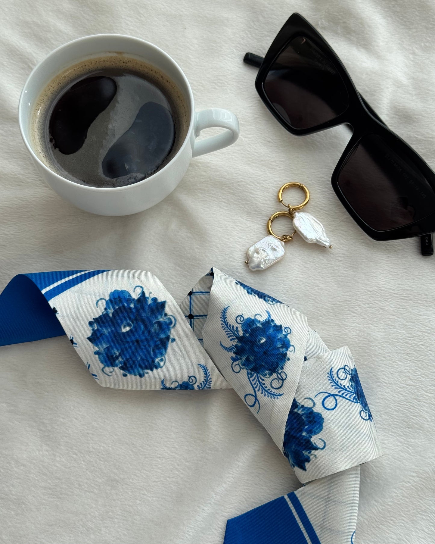 Sunglasses, coffee cup, and blue and white patterned scarf on a light surface