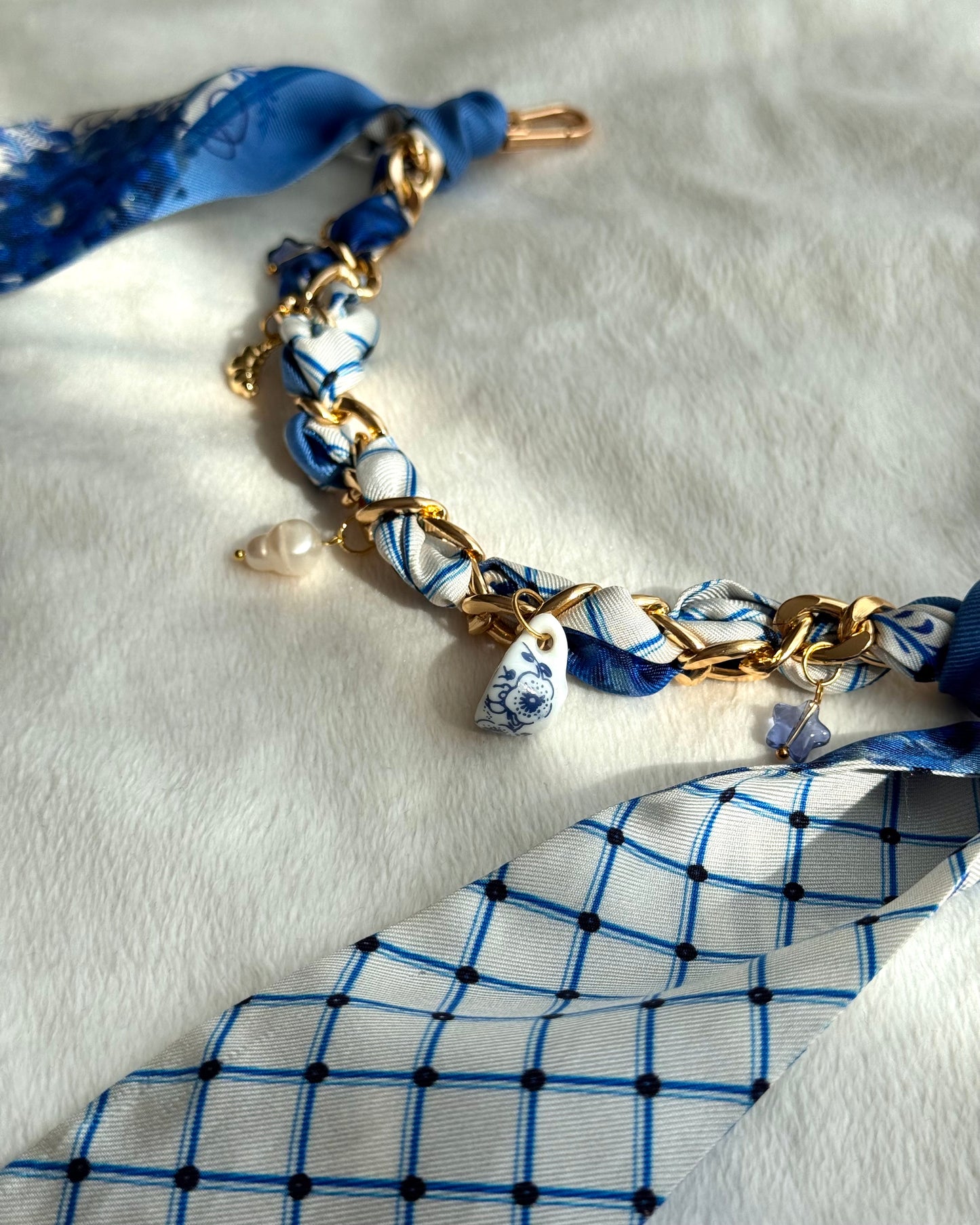 Bag charm with blue and white patterned fabric and gold chain on a white background